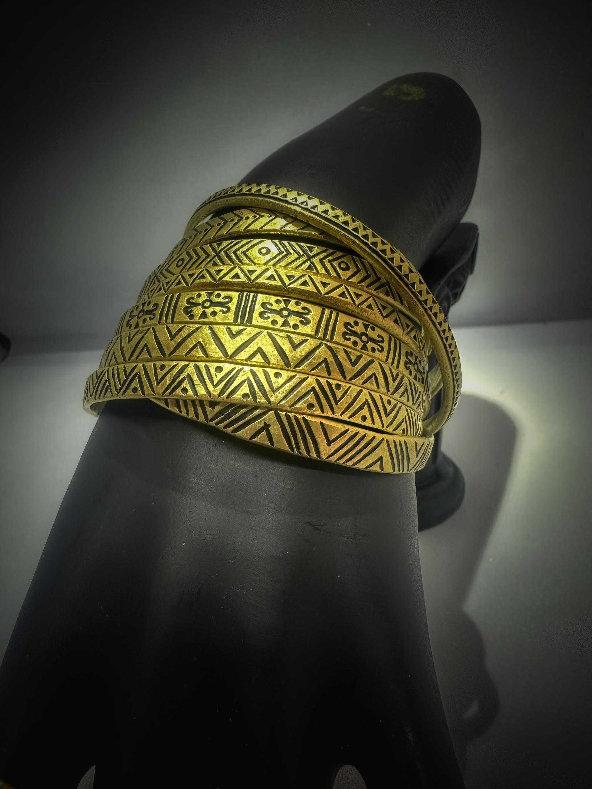 Stack of brass bracelets with diamond, chevron and floral patterns under warm light