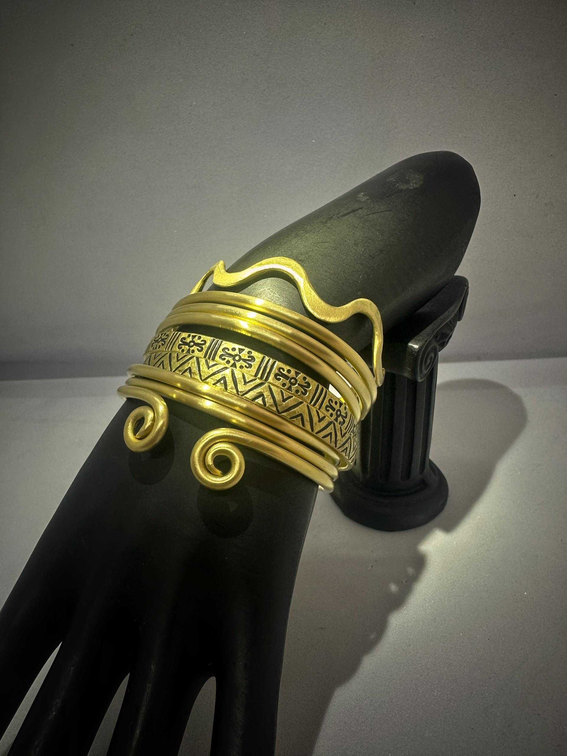 Brass cuff bracelet with spiral ends and etched motifs on a black display hand