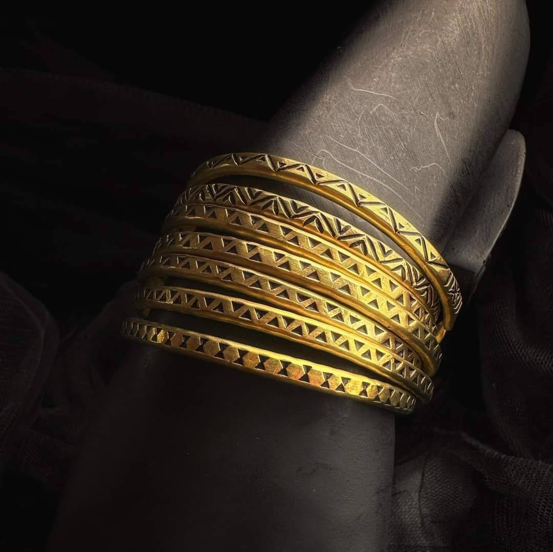 Stack of narrow brass bracelets with repeating triangular patterns in moody lighting